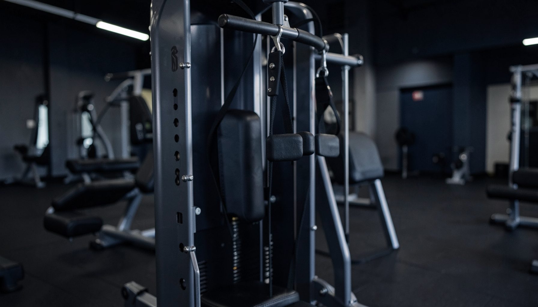 A cable machine with a handle set at chest height, muted gym lighting, deep navy and steel gray palette.