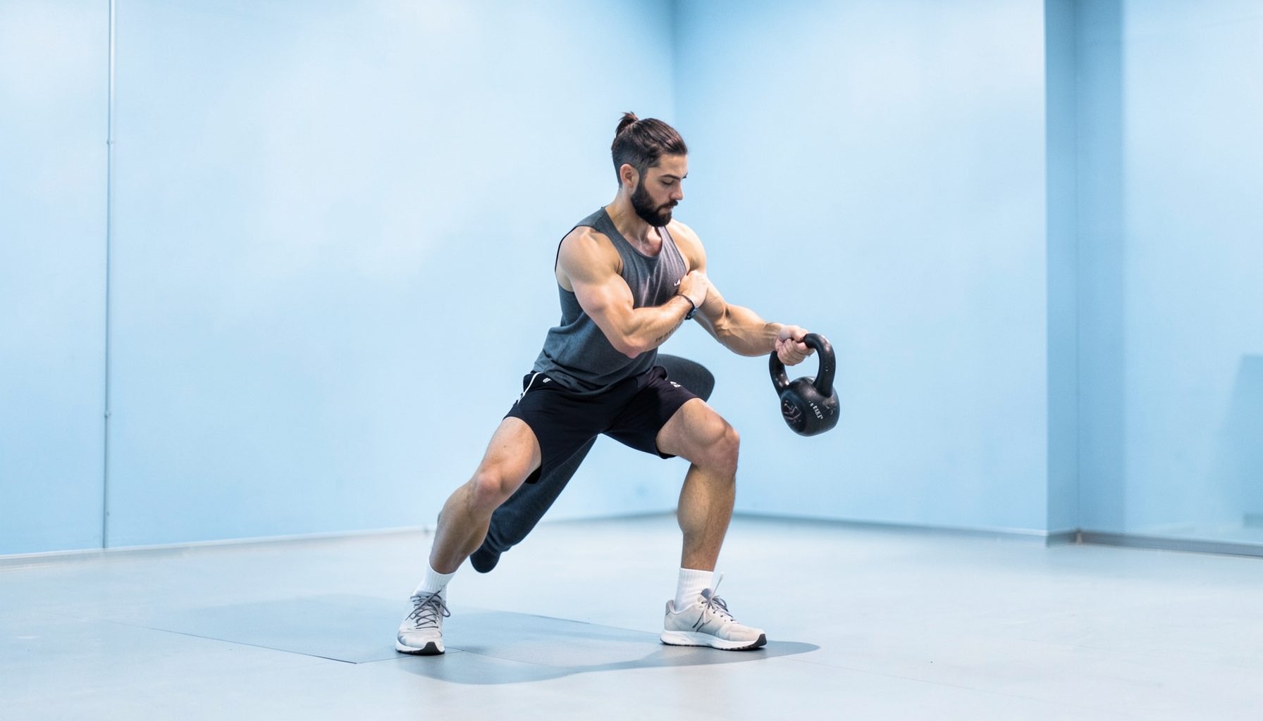 A person performing a single-leg Romanian deadlift with a kettlebell in a bright, minimalist gym, soft steel-blue walls